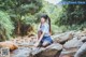 A woman sitting on a rock in the middle of a stream.